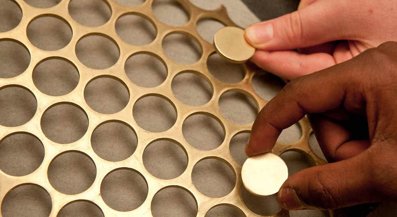 Two £1 coin blanks being held over the nickle-brass webbing they were cut from.